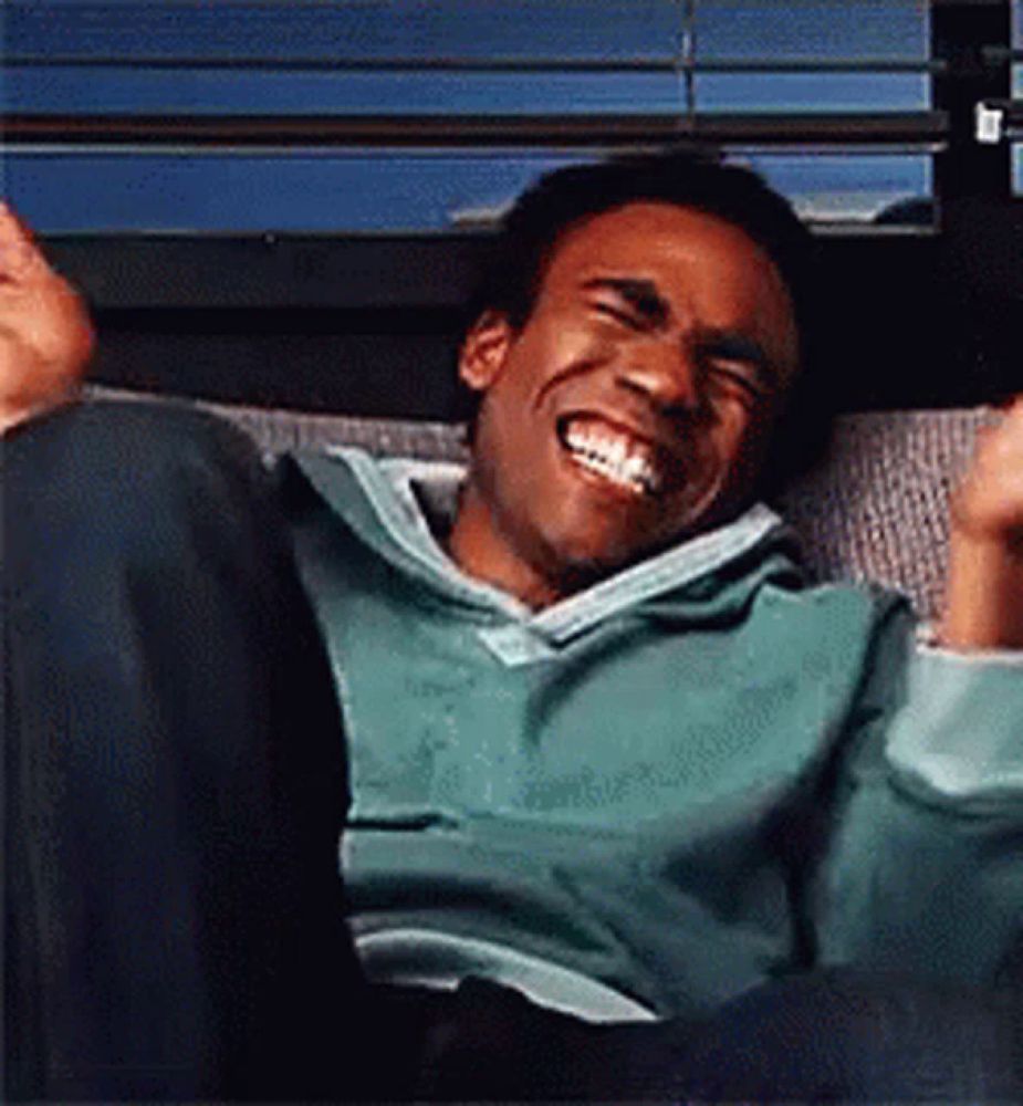 a man is sitting on a couch and laughing with his hands in the air .