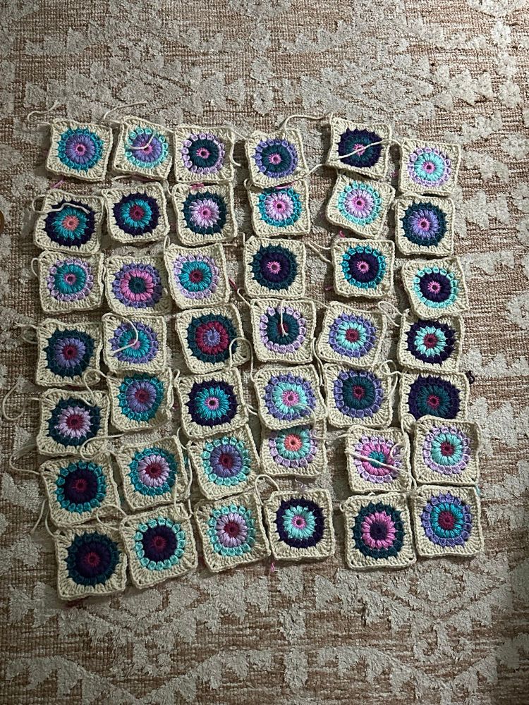 A bunch of individual granny squares in shades of blue, pink, purple, and off-white that will eventually be joined together into a blanket