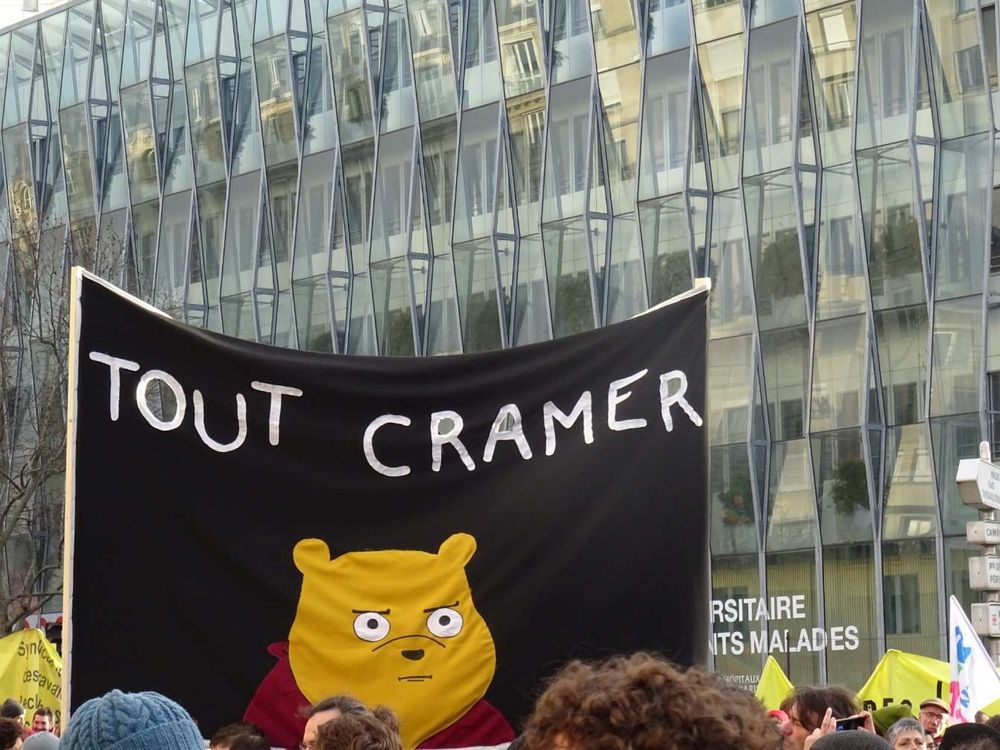 Grand drapeau brandi durant une manifestation. Sur ce drapeau noir est écrit en blanc "Tout Cramer" avec en dessous Winnie l'ourson en colère