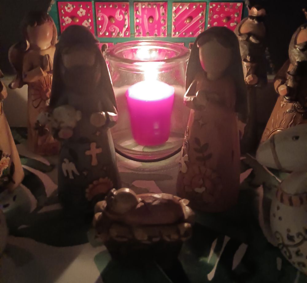 Photo of creche figures illuminated by a red candle.