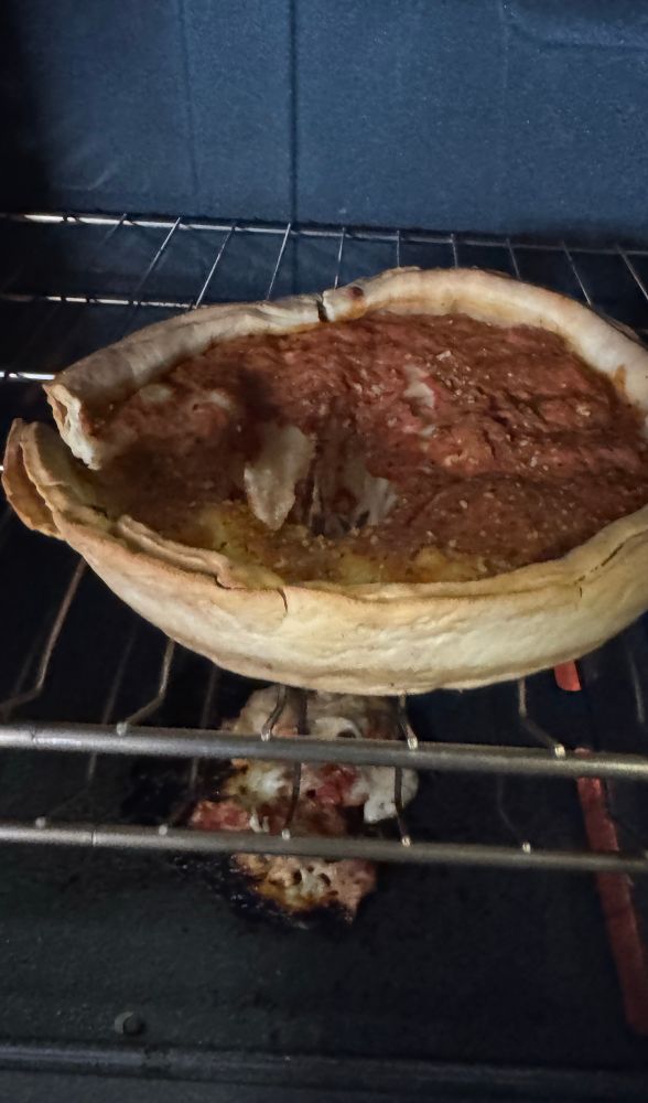 photo of a frozen deep dish pizza cooking in the oven, but the middle of the pizza apparently is too heavy for the crust and so the sauce and toppings have fallen through creating a big hole in the pizza 