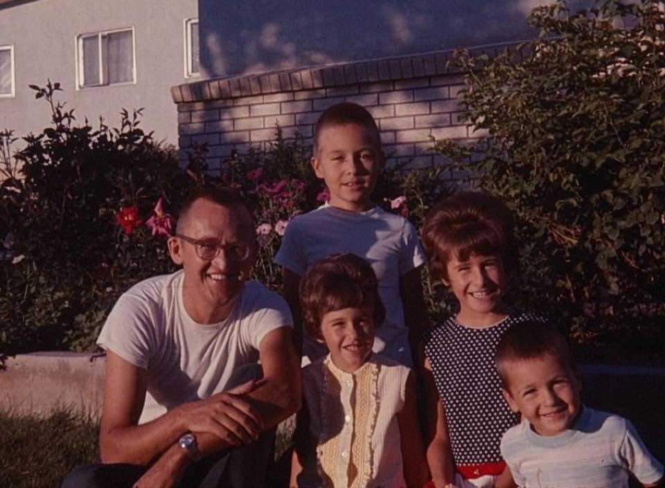 A childhood photo of Assemblymember Rick Chavez Zbur posing for a photo with his father and siblings in front of a home with a brick fence and bushes.