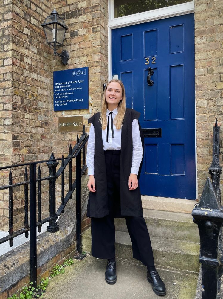 Moa is smiling and is standing in front of the Department of Social Policy and Intervention