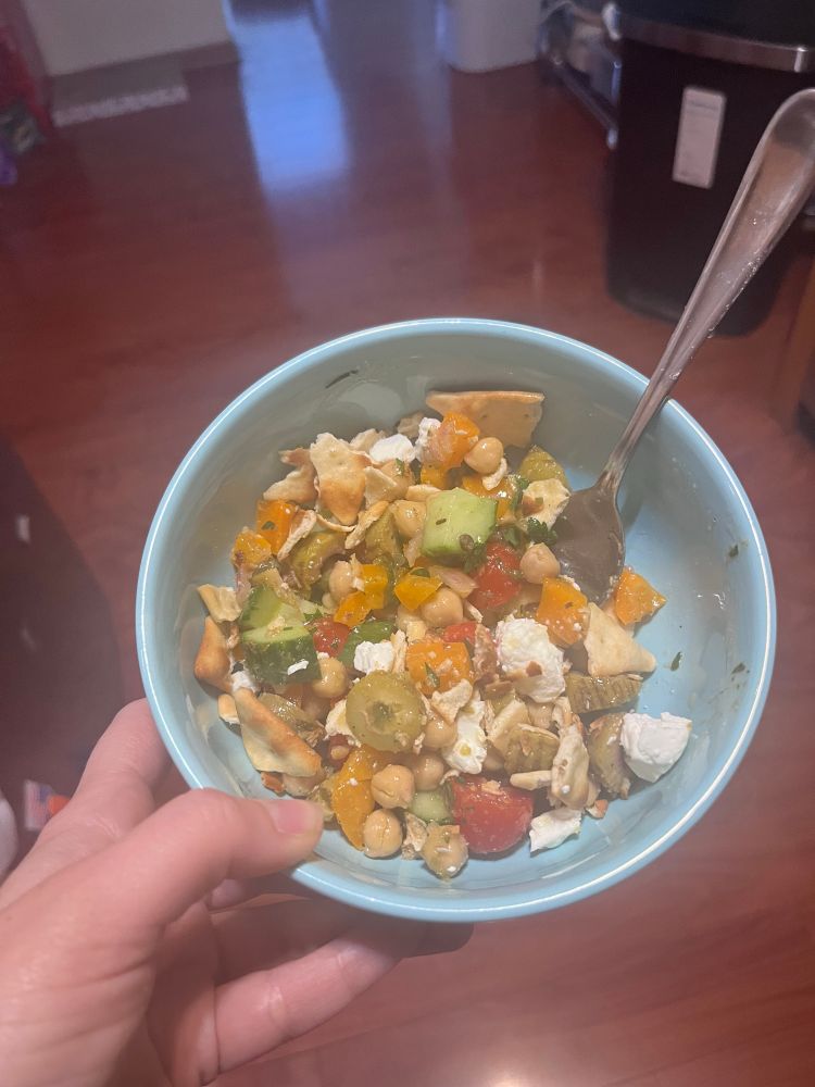 A bowl of salad with olives, feta, chickpeas, bell peppers, cucumbers, tomatoes, pita chips, and other yumminess. 