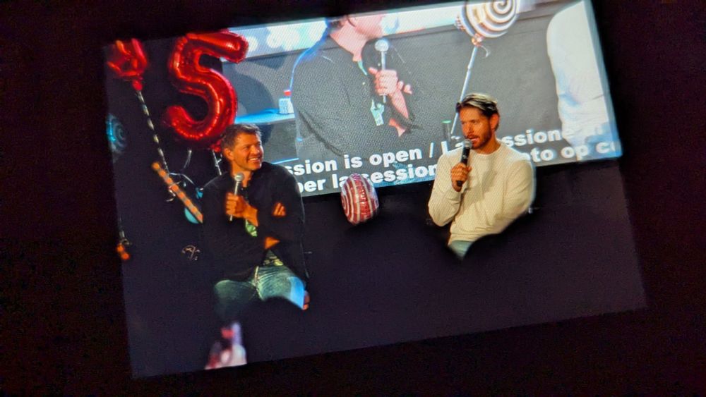 Misha and Jensen on stage. Jensen talking while Misha is listening