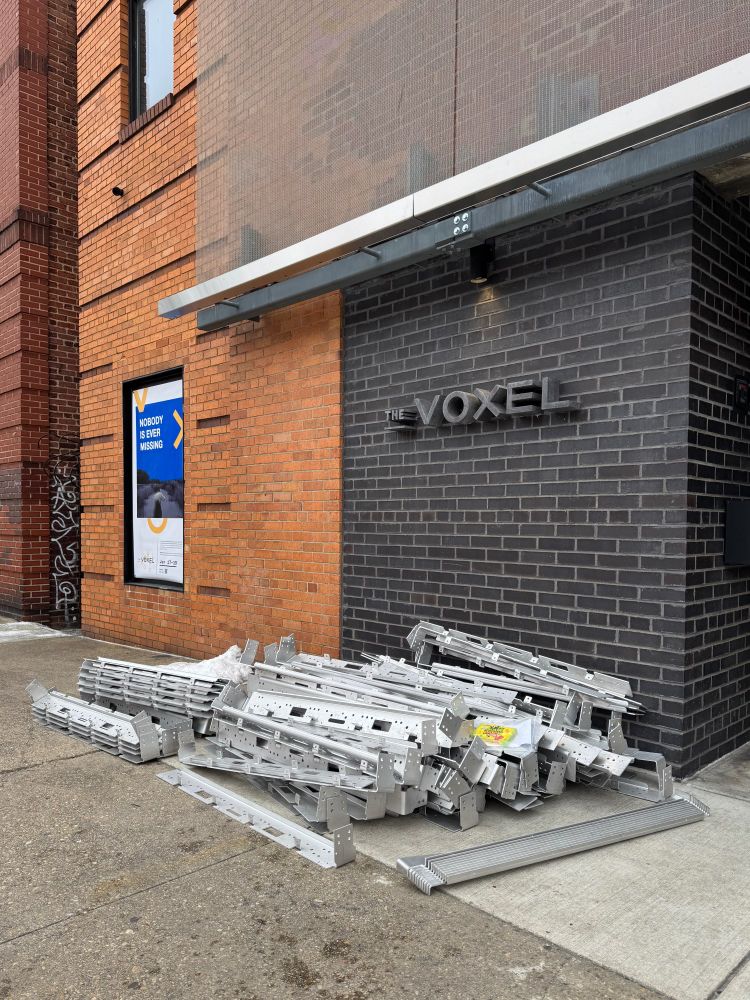 A pile of aluminum parts sitting outside, underneath the Voxel theater's sign.