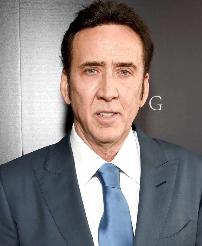 Nic cage in a grey suit blue tie short brown hair looking at the camera. hot. 