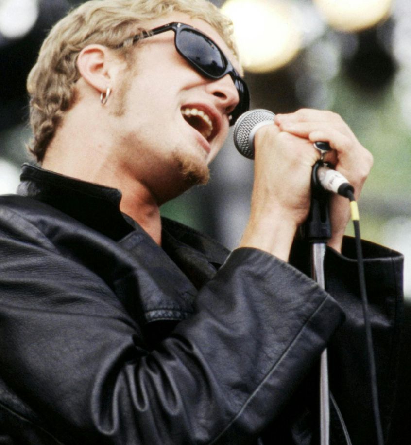 Layne Staley in a black leather jacket short blonde hair black shades singing into the mic. hot.