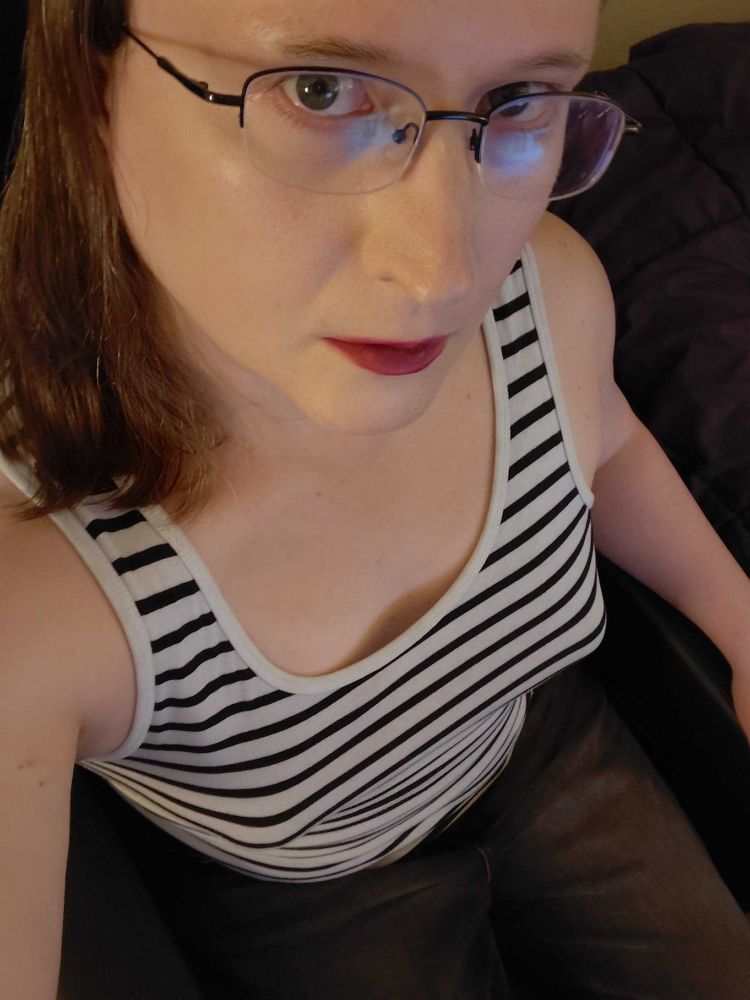 Sophia Nyx in a black and white stripe top black skinny jeans purple lipstick glasses long brown hair sitting in black chair looking up at cam. hot. meow.