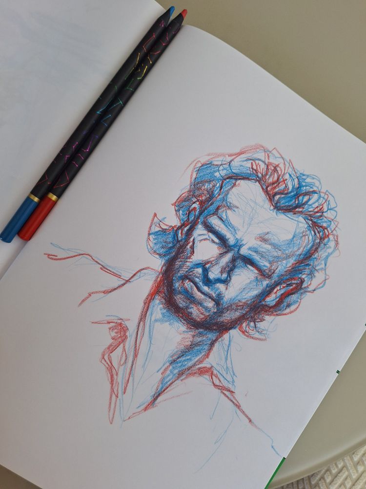 Caricatura de Andrew Lincoln, ator de The Walking Dead, num caderno e lápis de cor azul e vermelho aparecem sobre o caderno