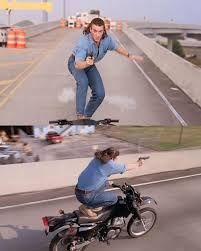 Van Damme se equilibrando em pé numa moto em alta velocidade, apontando um revólver. Ele usa um look all jeans e mullets.