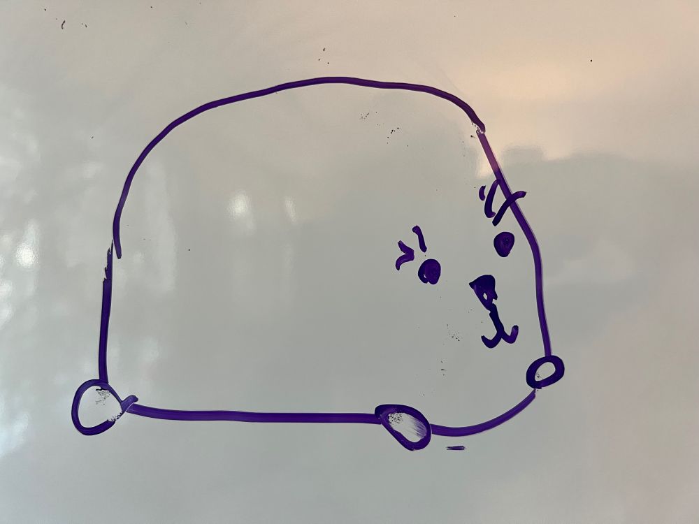 original Star Trek Lower Decks Moopsy design that looks like a load of bread with a face and feet. Purple dry erase marker on whiteboard.