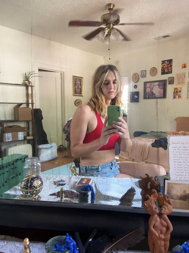 gwinnie mirror selfie wearing a read sports bra and denim shorts