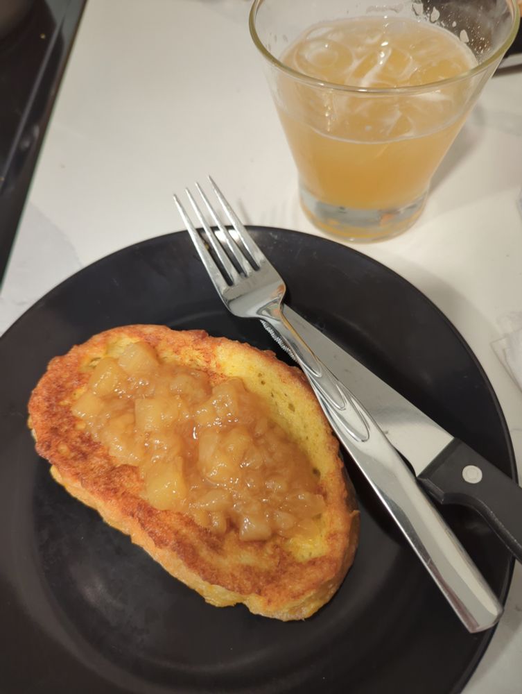 A plate of french toast with pineapple compote on top, there is a cocktail beside the plate. 