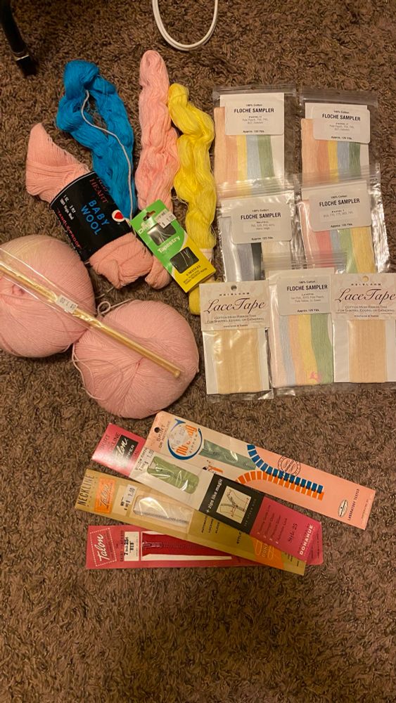 Thrift haul consisting of several skeins of floss/embroidery thread in multiple colors, three skeins of pink wool yarn, wooden knitting needles, two packs of lace tape and four vintage zippers. 