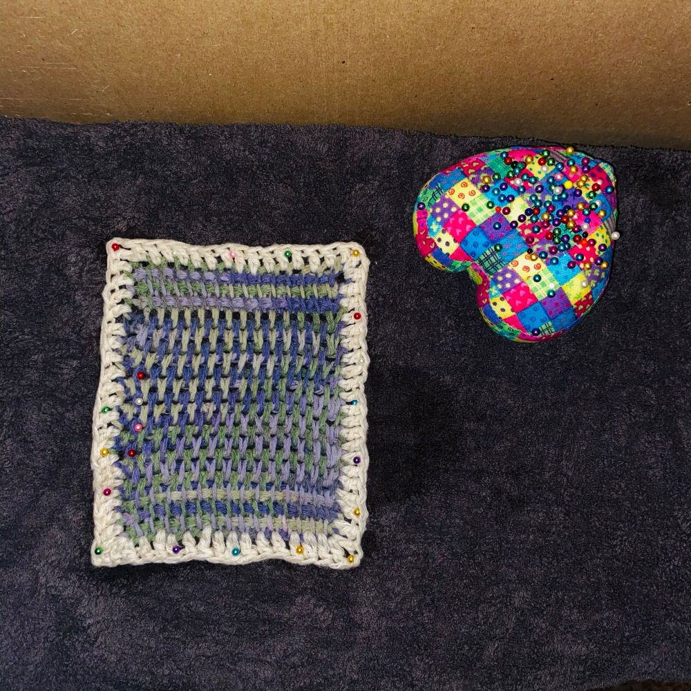 Wet blocked dish cloth. Pinned down with sewing pins (heart shaped pin cushion on the right) because that’s all I have. 