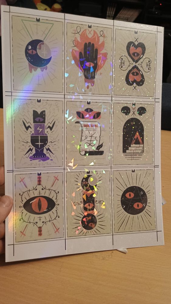 A new print of the Cult of the Lamb Tarot Cards from previous posts, printed more high quality and much more vibrant, with different laminating foil, each row having a different type. From left to right, each with three cards, there's Holographic, broken glass and stars.