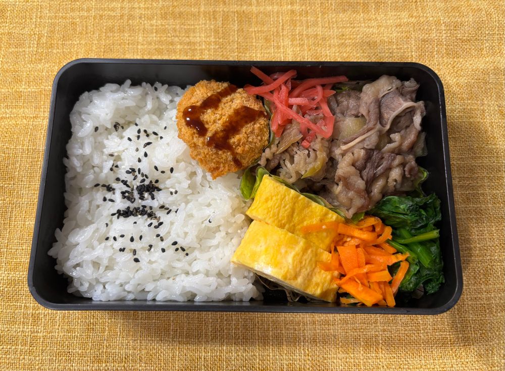 牛丼、卵焼き、人参ナムル、茹でほうれん草、冷凍ひとくちカツ、紅生姜がおかずのお弁当。ご飯にはごま塩。
