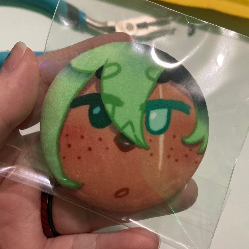 A closeup of the Monet Button. It has their bangs swooping in, with a cute, sort of bewildered expression on their face. 