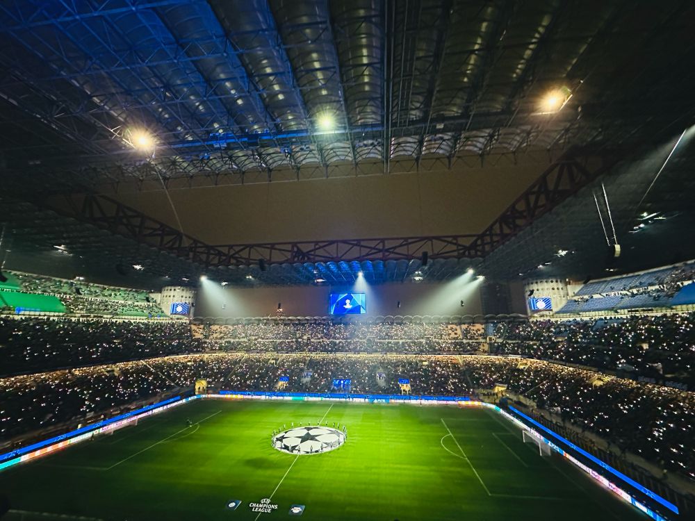 The San Siro before the Champions League game between Inter and RB Leipzig. The stadium lights are dimmed as the fans raise their phone torches. Like a Coldplay concert but with more Italian swear words. 
