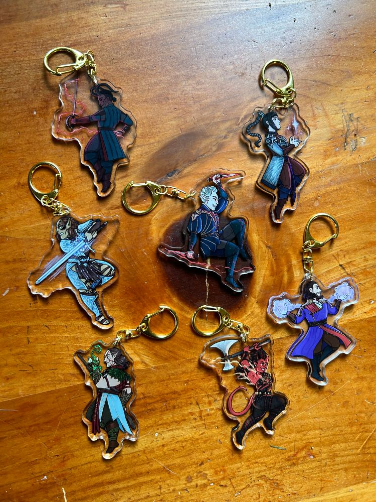 A collection of Baldur’s Gate 3 character keychains laid out on a wood table.
