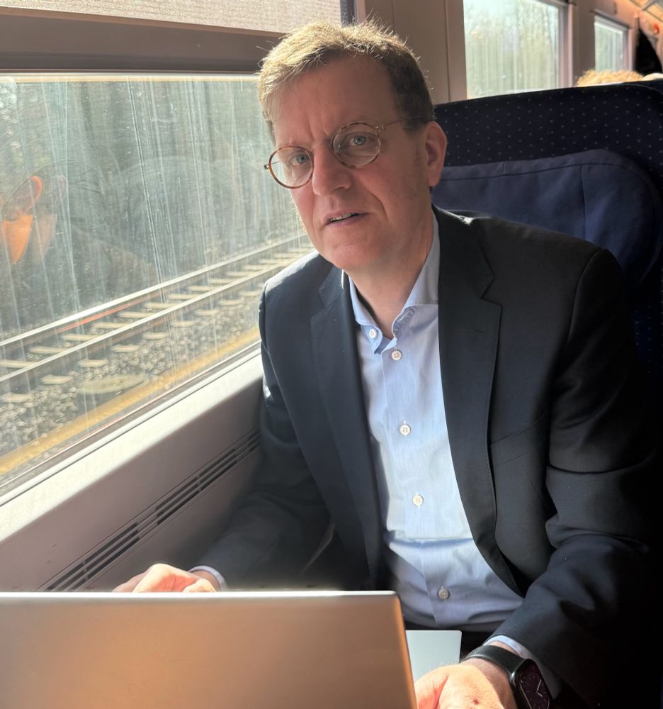 Elmar Bartlmae sitting in a train in front of a laptop. The sun is shining.