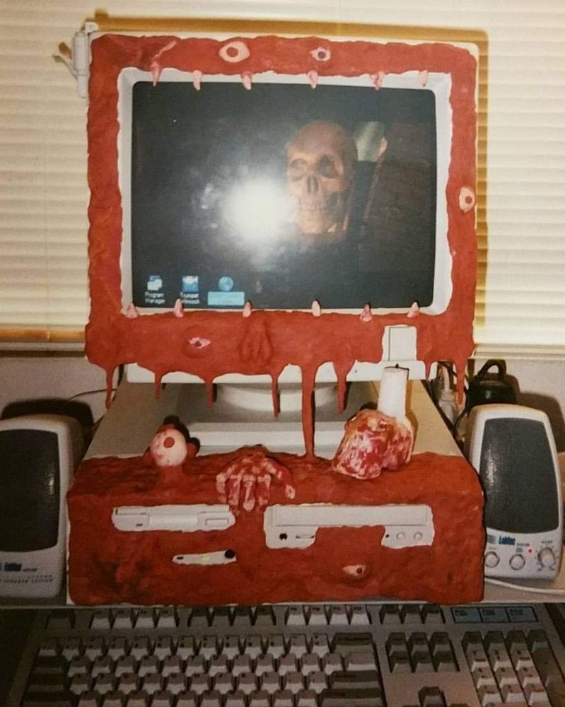 Picture of a late 90s desktop with red clay pressed to the front of the case and monitor, with strange shapes, white clay eyes and teeth.