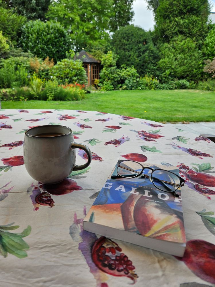A copy of Alison Brackenbury's selected poems, "Gallop", with a big cup of coffee and a pair of glasses on a garden table. 