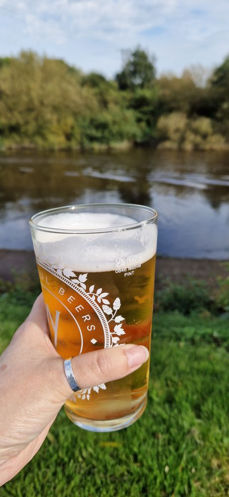 A hand clutching a lovely pint of beer by a river. 