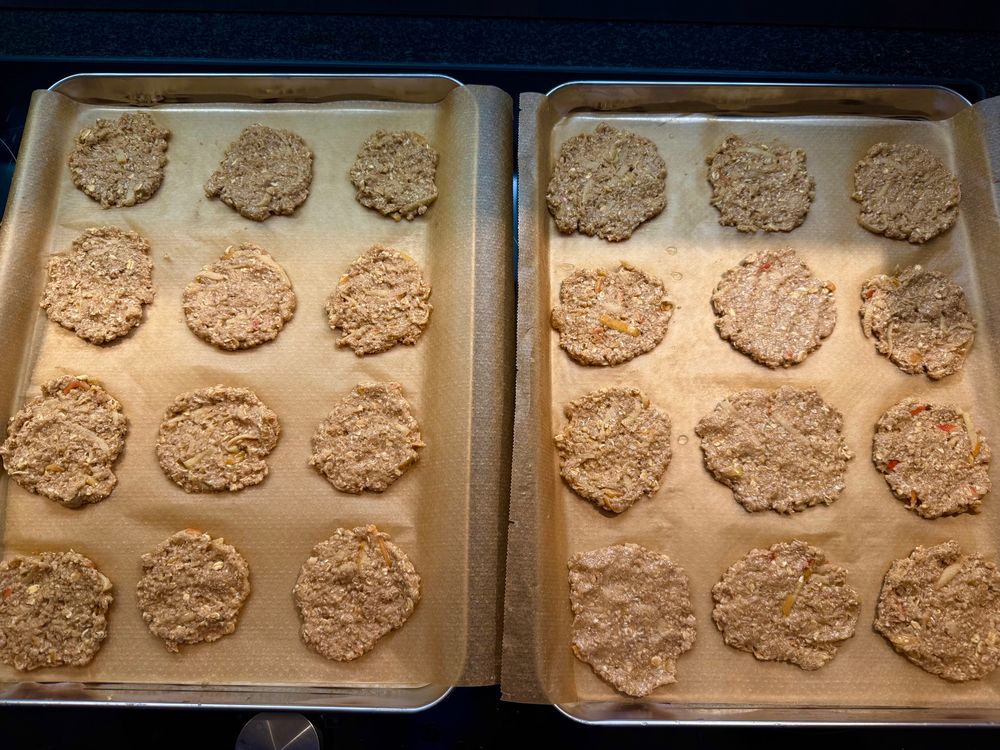Zwei Bleche mit Backpapier und ungebackenen Haferkeksen