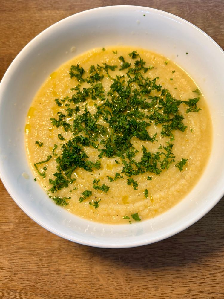 Blumenkohl Suppe dekoriert mit Petersilie und Olivenöl in einem weißen Teller auf einem Holztisch 