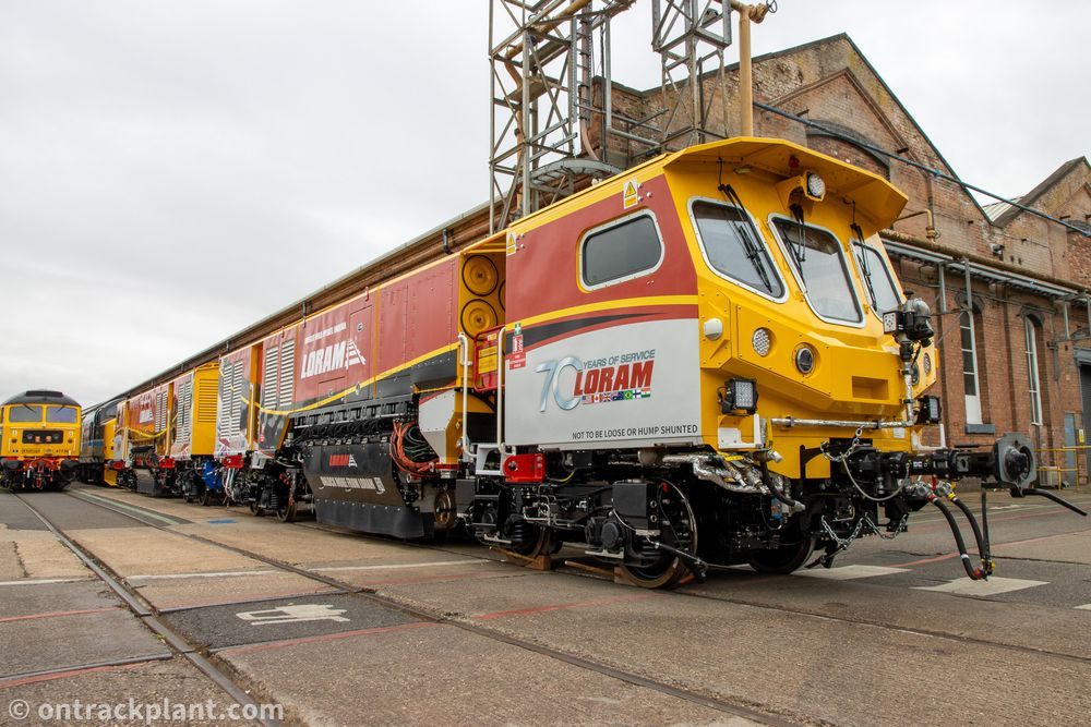 a low-angle photo of a red, white and yellow railway grinding machine