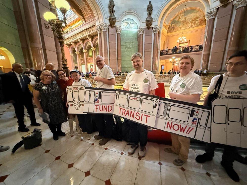 Transit advocates wearing cardboard train in Springfield that reads "FUND TRANSIT NOW!!"