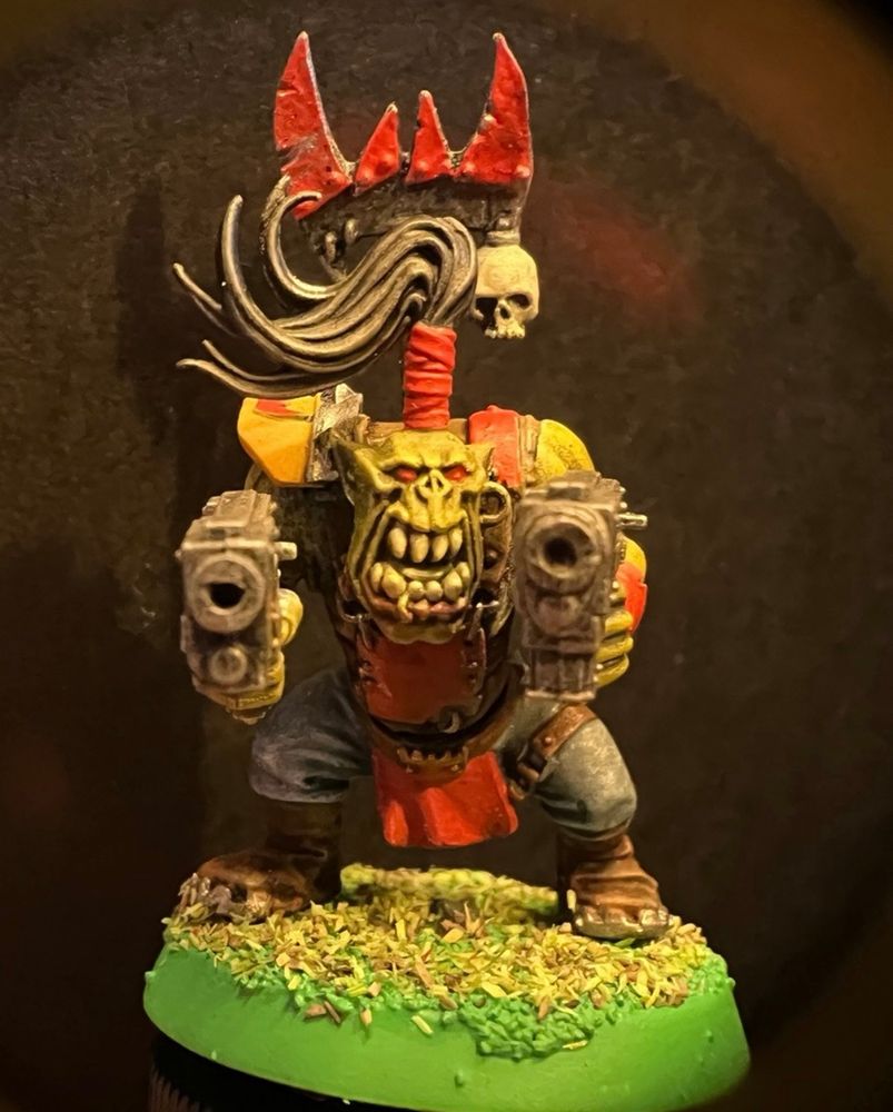 Ork with high topknot armed with twin pistols and standing on a grassy base with goblin green rim. 