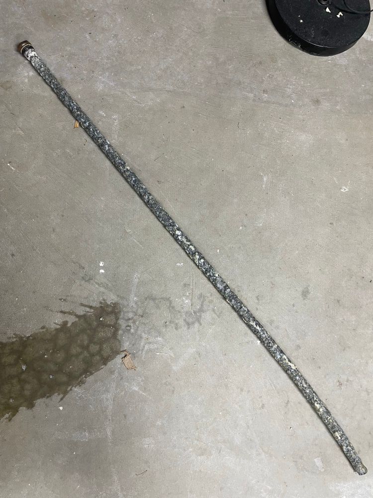A long grey rod from a water heater, corroded and broken down with age. It sits on a grey concrete floor.