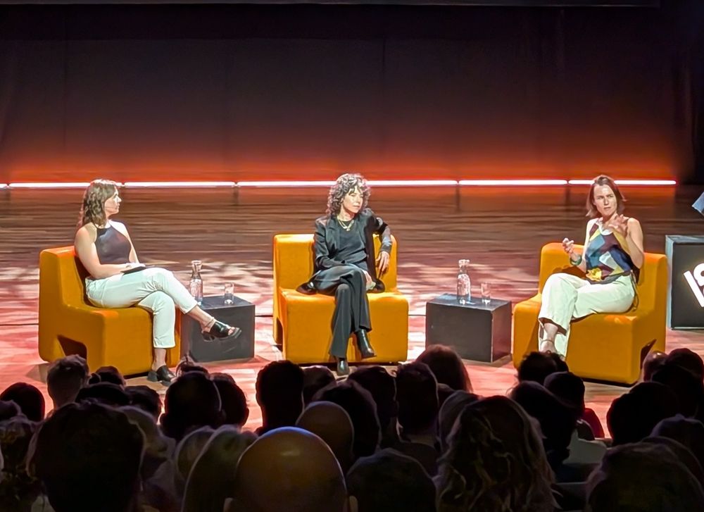 Three ladies on a stage, comfortably seated, gesturing while talking