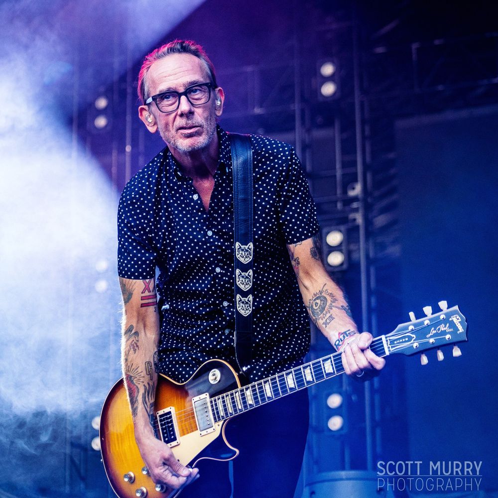 Brian Baker arched slightly over guitar with satisfied expression during a Bad Religion set at Chicago’s Riot Fest.