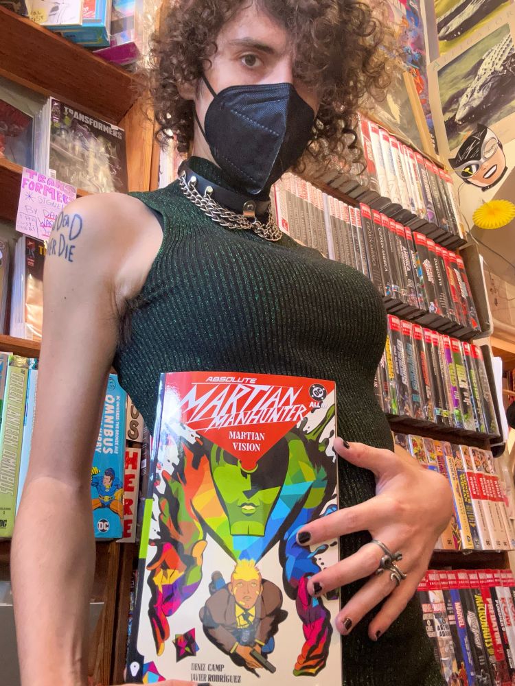 A big boobed baddie in a green dress holding up a copy of Martian Manhunter volume 1