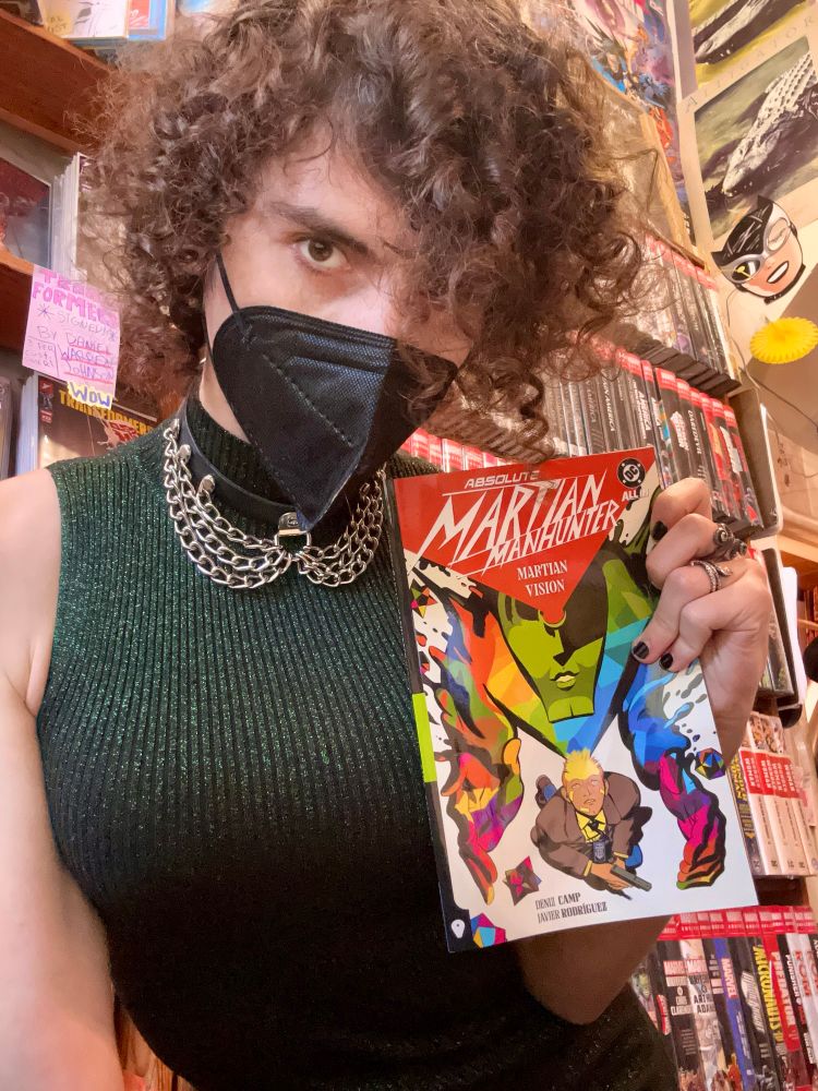 A big boobed baddie in a green dress holding up a copy of Martian Manhunter volume 1 but closer up and a different pose