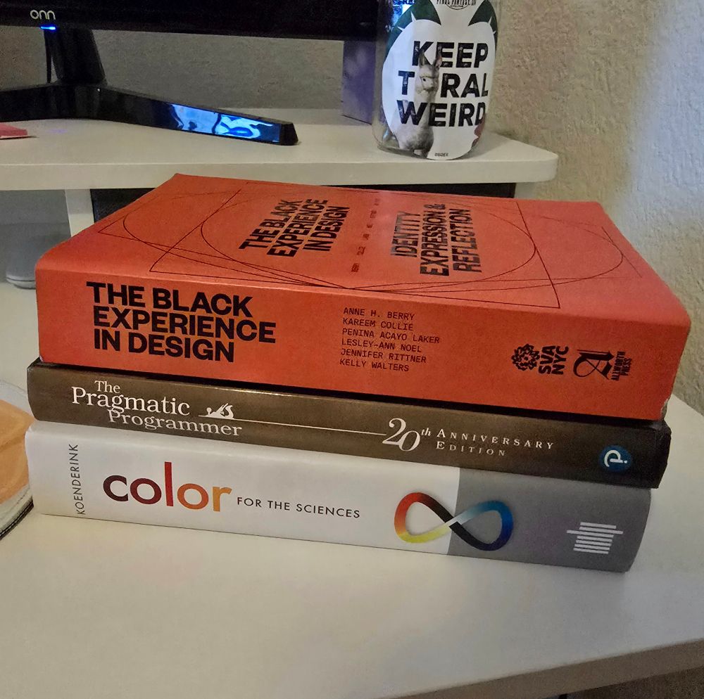 Stack of three books on a desk. Books are The Black Experience in Design, The Pragmatic Programmer, and Color for the Sciences. 