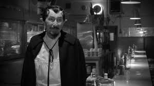 In black and white a man in a cafe wearing a cape and looking like a vampire