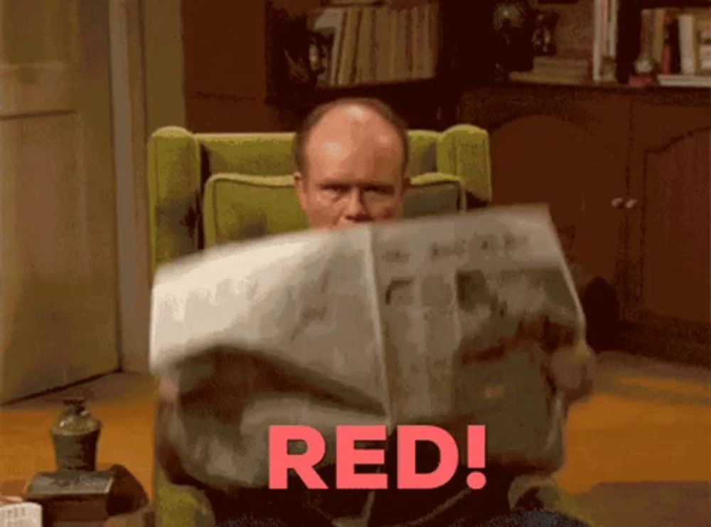 a man sitting in a chair reading a newspaper with the word red on the bottom