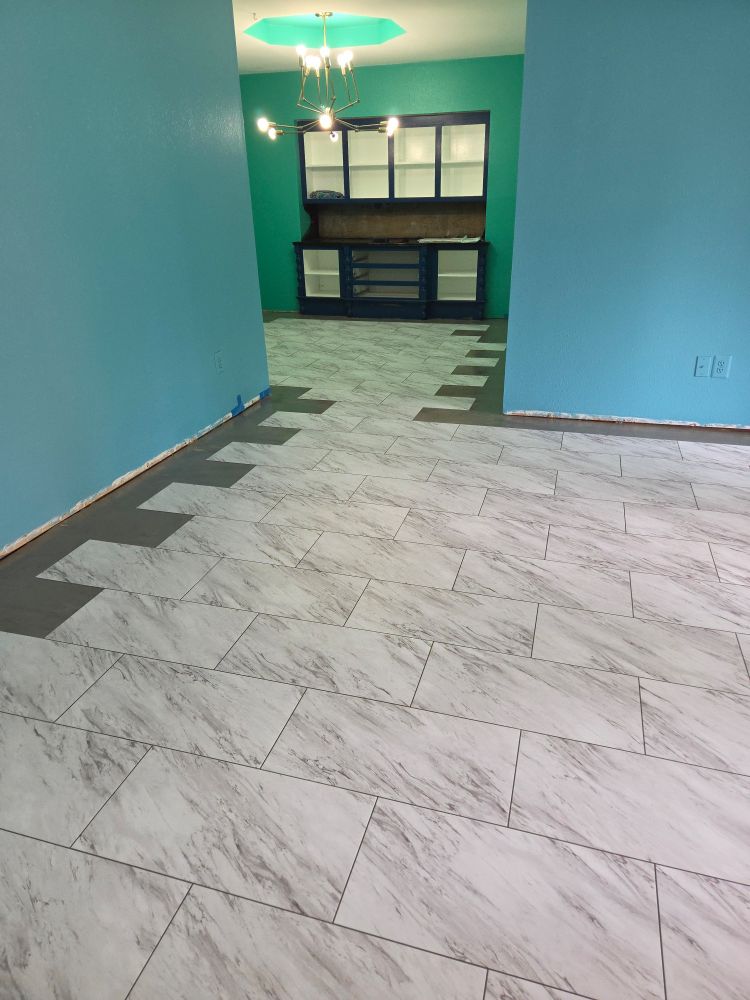A blue walled room opens into a green walled room with a built in cabinet missing it's doors. A white and gray marble tile is laid out in both rooms everywhere but the perimeter.