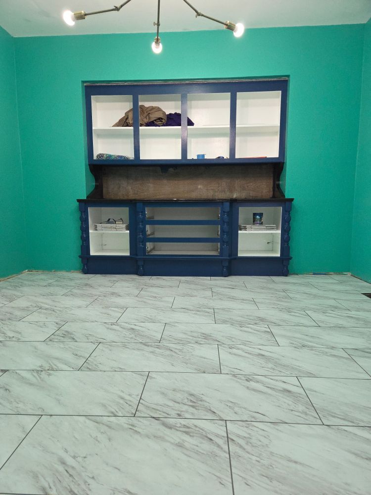 A green room with a navy blue built in cabinet without drawers or cabinet doors and a vinyl tile floor with a white and gray marble pattern