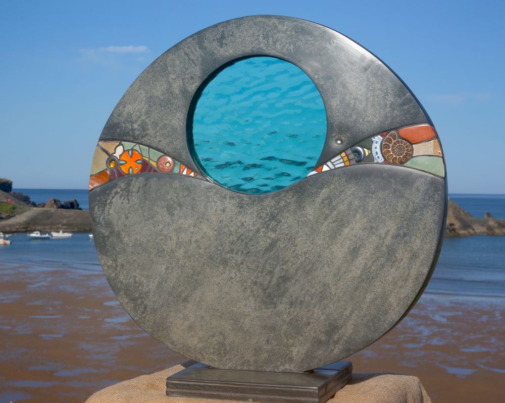 Sculpture with slate and blue glass with a band of decoration including fossils and gems