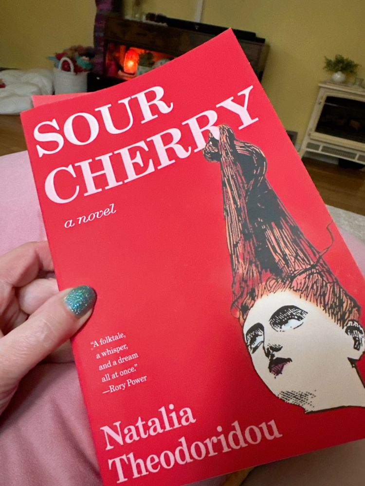 Photo of a paperback book with a red cover and a woman’s head called Sour Cherry by Natalia Theodoridou 