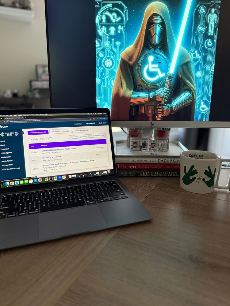 Computer desk with screen open to axe-con, a asl coffee mug to the right of the computer and larger adapted computer screen with an a11y Jedi on it 