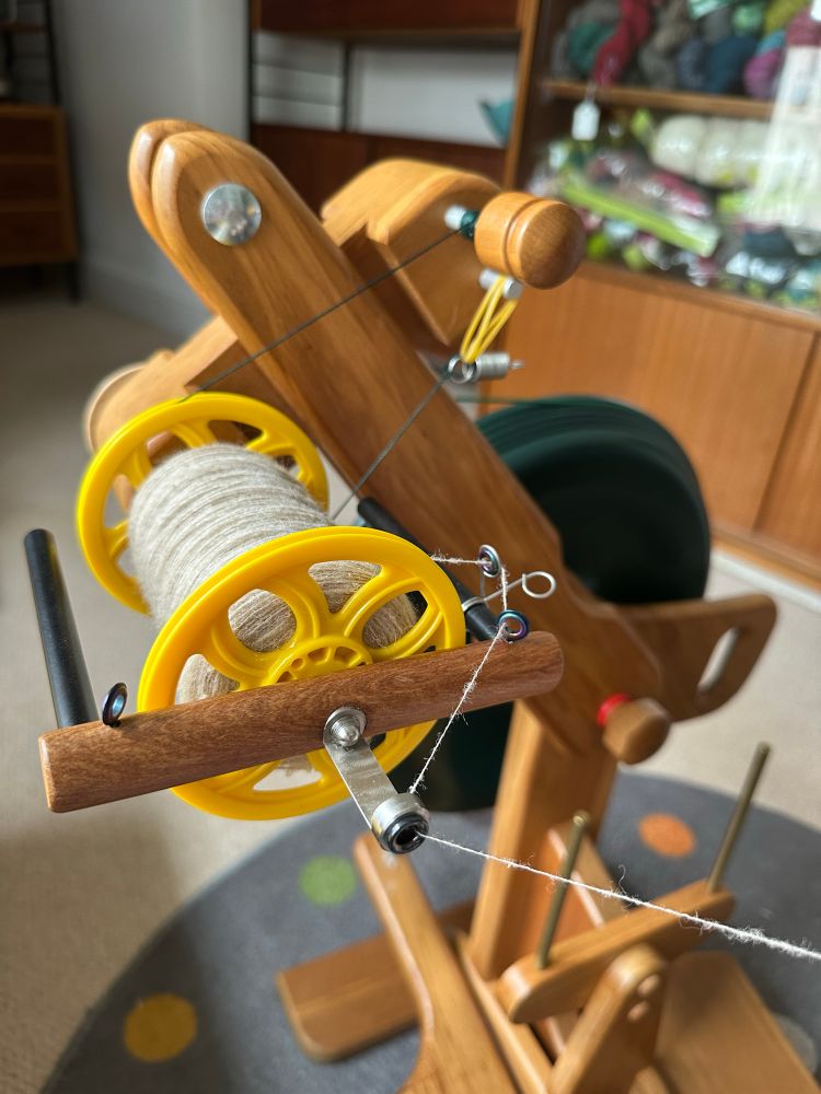 A bright yellow bobbin 3/4 full of creamy white, woollen spun singles on a Majacraft Suzie Pro spinning wheel. 