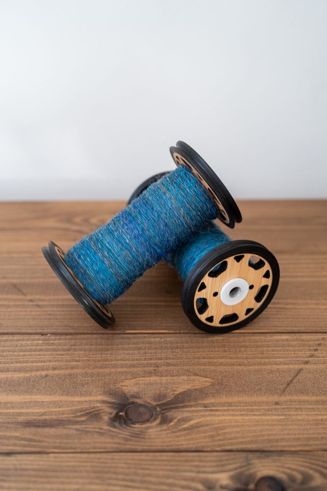Two bobbins part-full of a complex mid-blue yarn. 