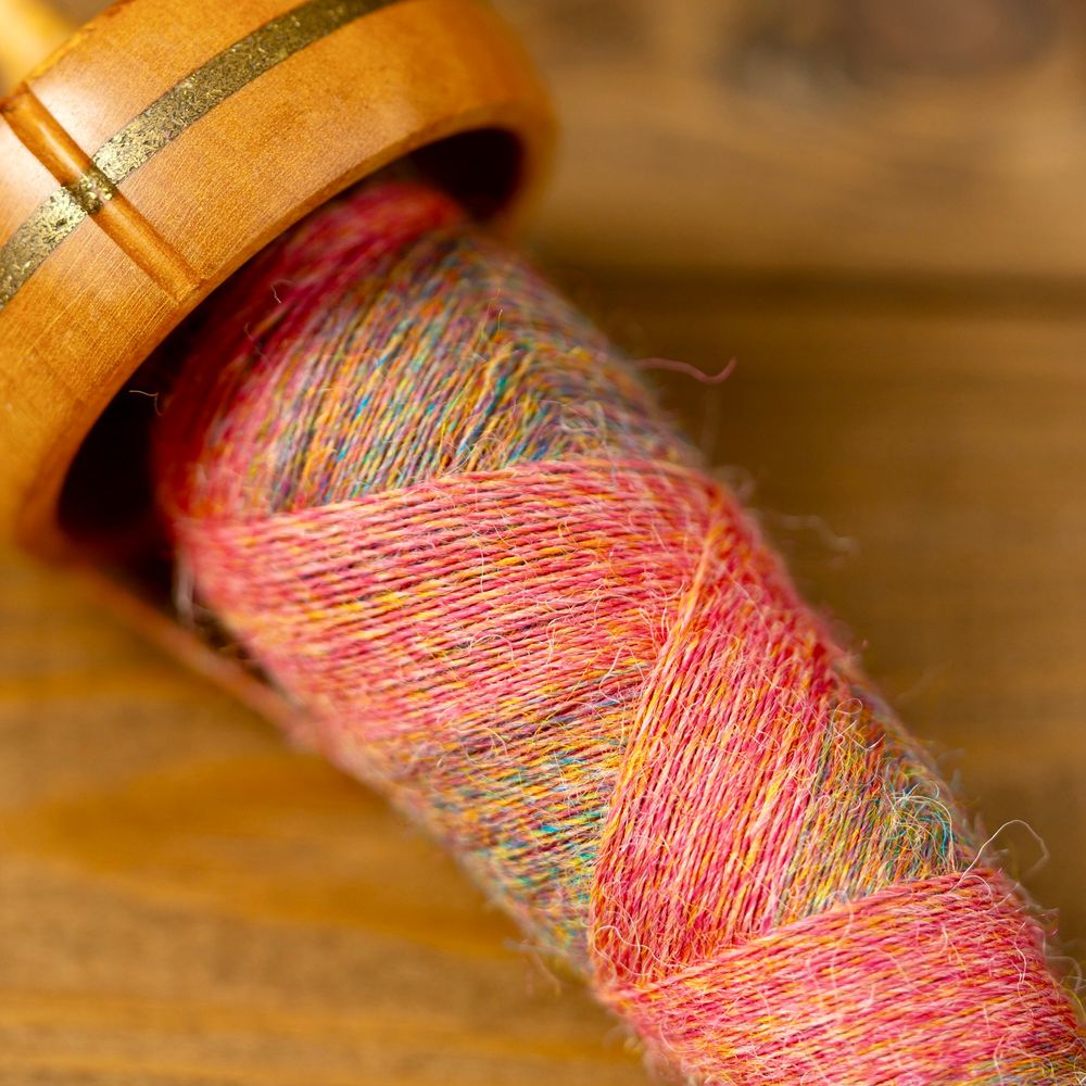 A spindle cop wound with multiple crosses so the multi-coloured singles change to a muted coral in a zig-zag. 